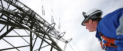 Mann blauer Overoll + Helm vor Hochspannungsmast Mann blauer Overoll + Helm vor Hochspannungsmast