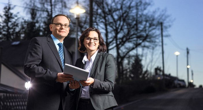 enviaM-Kommunalbetreuer Reginald Fuchs steht mit einer Frau in einer Straße mit leuchtenden Straßenlaternen enviaM-Kommunalbetreuer Reginald Fuchs steht mit einer Frau in einer Straße mit leuchtenden Straßenlaternen