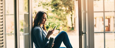 Studentin sitzt mit einem Smartphone in der Hand am Fenster Studentin sitzt mit einem Smartphone in der Hand am Fenster