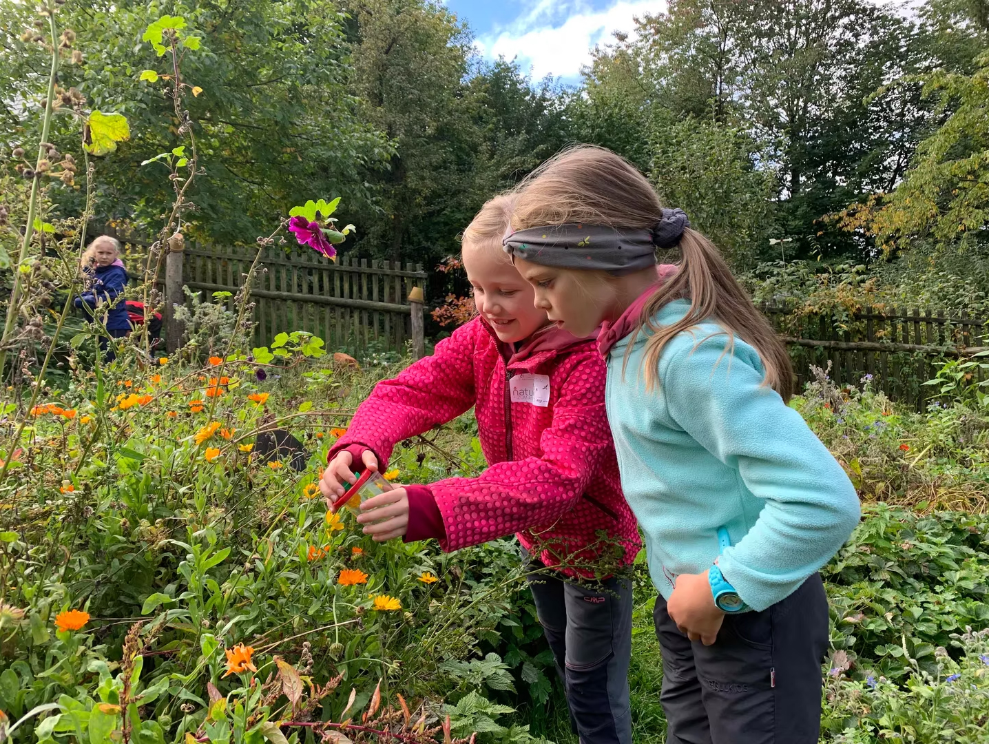 zwei Mädchen in einem blühenden Garten mit einer Becherlupe