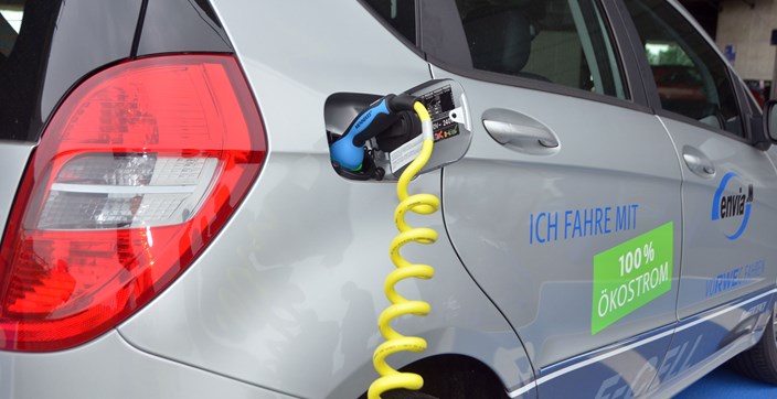 Heckansicht eines Elektrofahrzeugs das gerade an einem Ladekabel hängt Heckansicht eines Elektrofahrzeugs das gerade an einem Ladekabel hängt