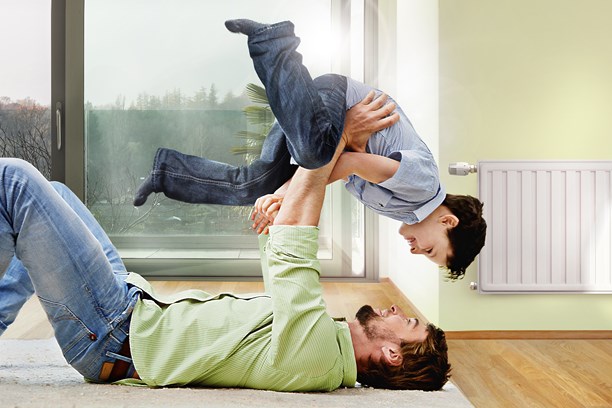 Vater liegt vor einem Heizkörper mit dem Rücken auf dem Boden und stemmt den Sohn spielerisch in die Luft Vater liegt vor einem Heizkörper mit dem Rücken auf dem Boden und stemmt den Sohn spielerisch in die Luft